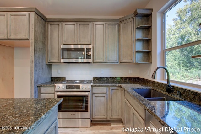 kitchen with sink, stainless steel appliances, dark stone counters, and light hardwood / wood-style flooring