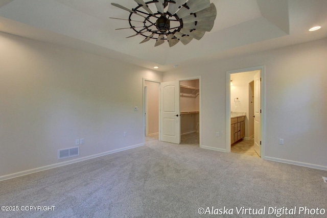 unfurnished bedroom featuring ensuite bathroom, light colored carpet, a tray ceiling, a walk in closet, and a closet