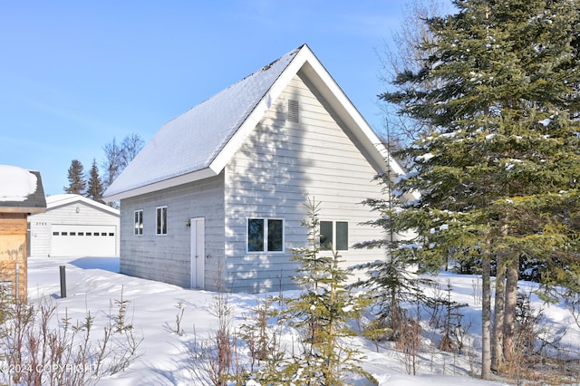 snow covered property with a garage and an outdoor structure