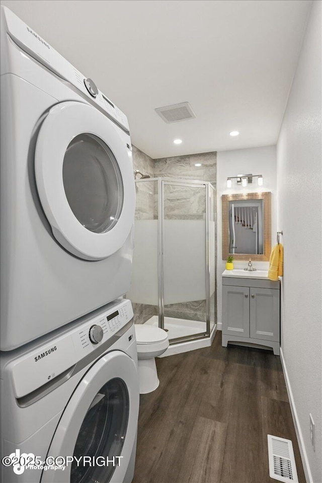 washroom with stacked washing maching and dryer, dark wood-type flooring, and sink