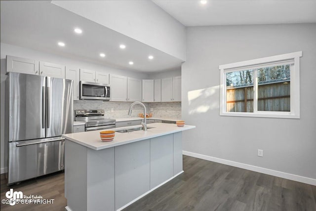 kitchen featuring decorative backsplash, appliances with stainless steel finishes, vaulted ceiling, a kitchen island with sink, and sink