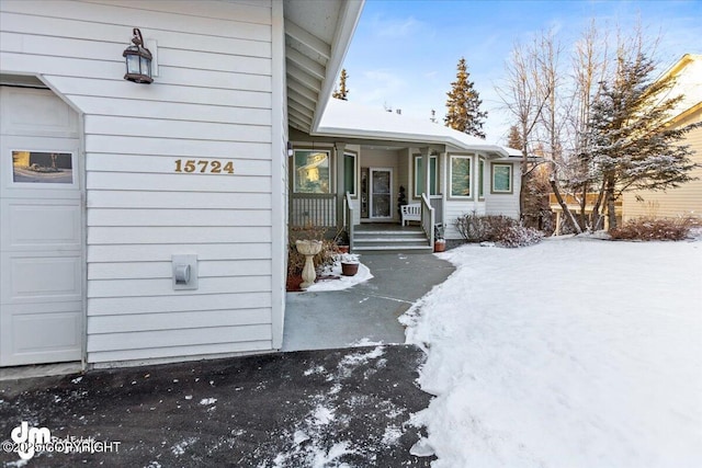 snow covered property entrance with covered porch and a garage