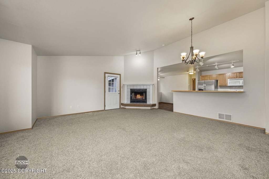 unfurnished living room featuring carpet flooring, a notable chandelier, a tile fireplace, and track lighting