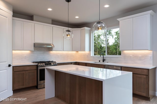 kitchen featuring sink, stainless steel appliances, decorative light fixtures, a kitchen island, and light wood-type flooring