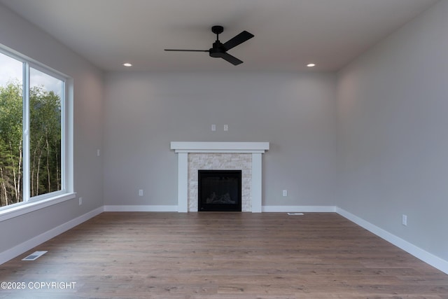 unfurnished living room with hardwood / wood-style floors, ceiling fan, and a stone fireplace