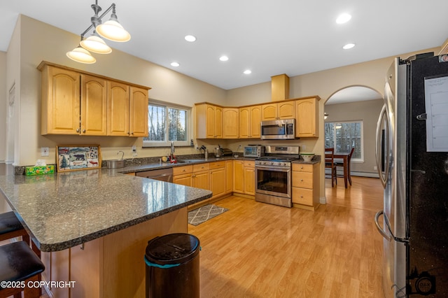 kitchen with a kitchen bar, kitchen peninsula, appliances with stainless steel finishes, decorative light fixtures, and sink