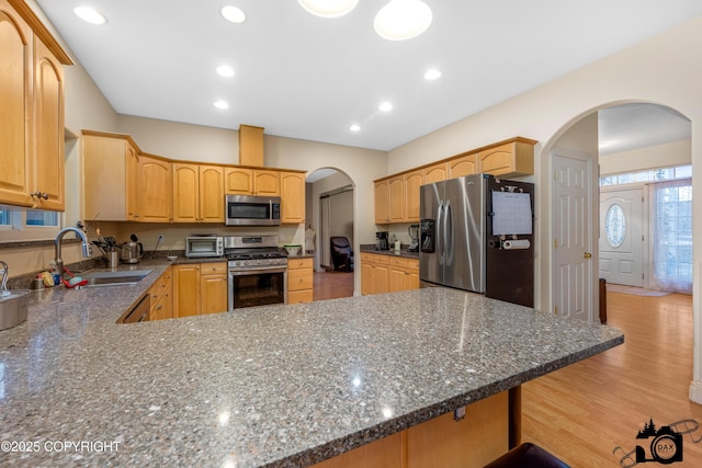 kitchen featuring stainless steel appliances, dark stone countertops, kitchen peninsula, and sink