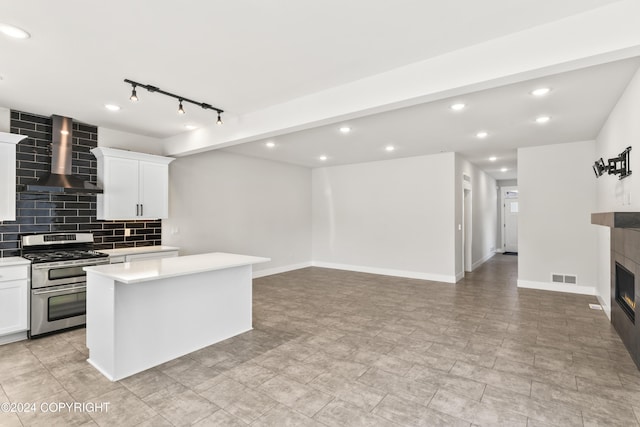 kitchen with a fireplace, a kitchen island, wall chimney range hood, white cabinets, and stainless steel range with gas cooktop