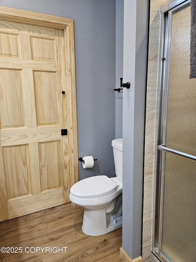 bathroom featuring toilet, a shower with shower door, and wood-type flooring