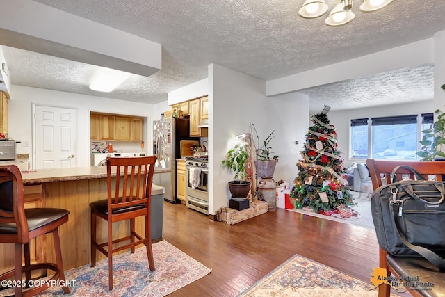 kitchen with a textured ceiling, dark hardwood / wood-style floors, a breakfast bar, and appliances with stainless steel finishes