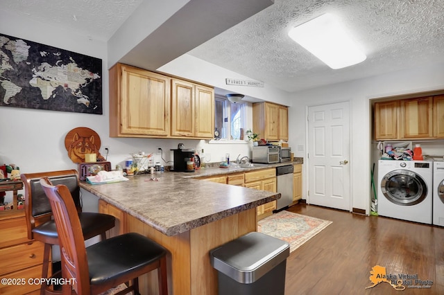 kitchen with kitchen peninsula, a kitchen breakfast bar, stainless steel dishwasher, a textured ceiling, and washer and clothes dryer