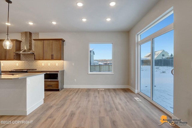 8803 Chalk Hill Loop, Anchorage, AK 99502 - kitchen featuring wall chimney range hood, light wood-style flooring, decorative backsplash, stainless steel microwave, and brown cabinets