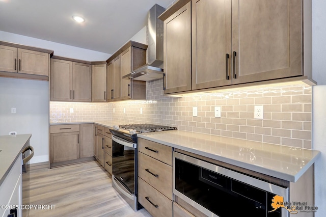 8803 Chalk Hill Loop, Anchorage, AK 99502 - kitchen with stainless steel appliances, wall chimney range hood, light wood-style flooring, decorative backsplash, and light countertops
