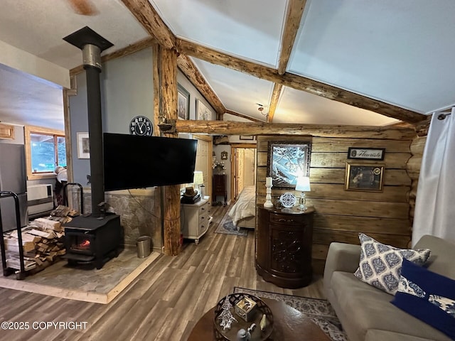 living room with vaulted ceiling with beams, wood walls, a wood stove, and hardwood / wood-style flooring