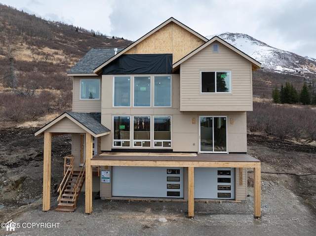 rear view of property with a shingled roof, stairs, a mountain view, and a garage