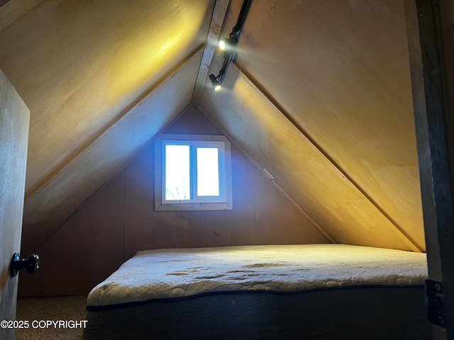 bedroom featuring vaulted ceiling, wood walls, and track lighting