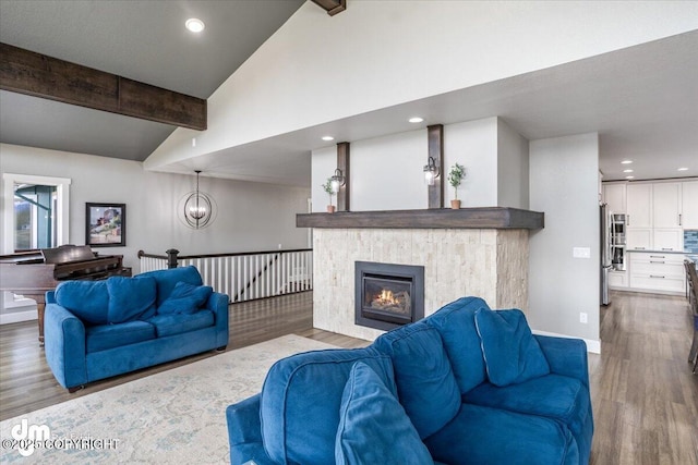 living room featuring lofted ceiling with beams, an inviting chandelier, light wood-type flooring, and a tiled fireplace