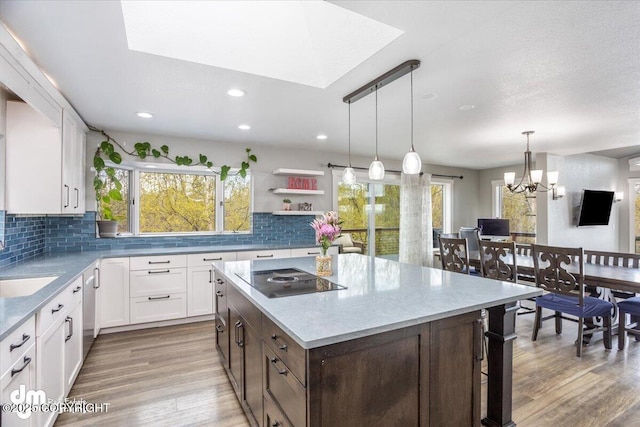 kitchen featuring backsplash, black electric cooktop, a kitchen island, and an inviting chandelier