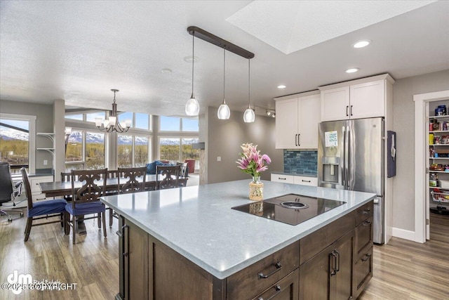 kitchen with stainless steel fridge with ice dispenser, backsplash, decorative light fixtures, black electric cooktop, and white cabinets