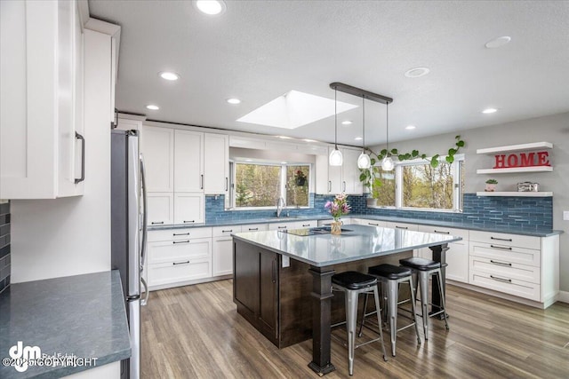 kitchen featuring a breakfast bar, a skylight, a kitchen island, white cabinetry, and stainless steel refrigerator