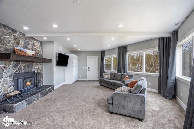 living room with a stone fireplace, beamed ceiling, and carpet