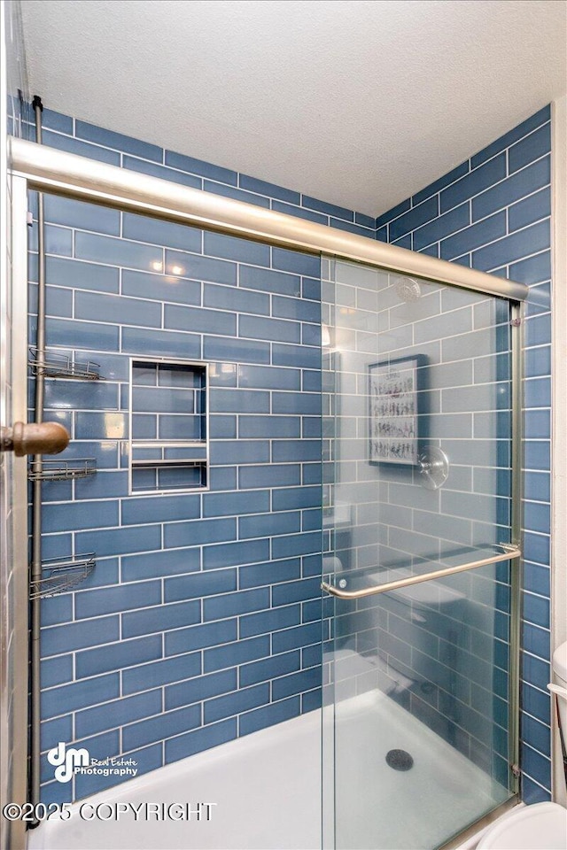 bathroom featuring toilet, a shower with door, and a textured ceiling