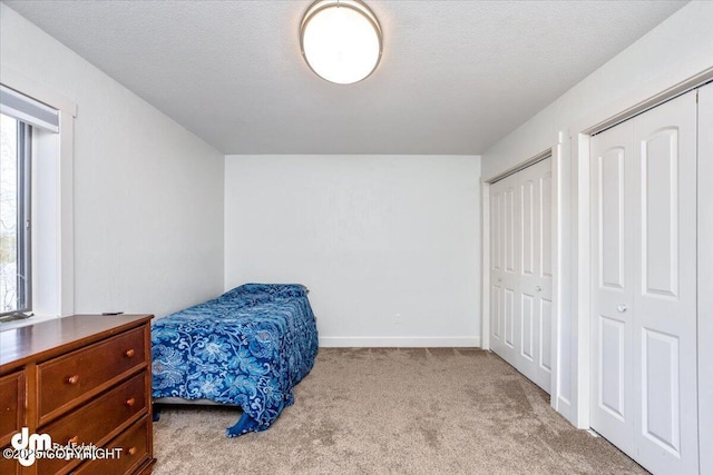 bedroom featuring a textured ceiling, light colored carpet, and two closets