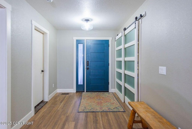 entryway with a textured ceiling, a barn door, and dark wood-type flooring