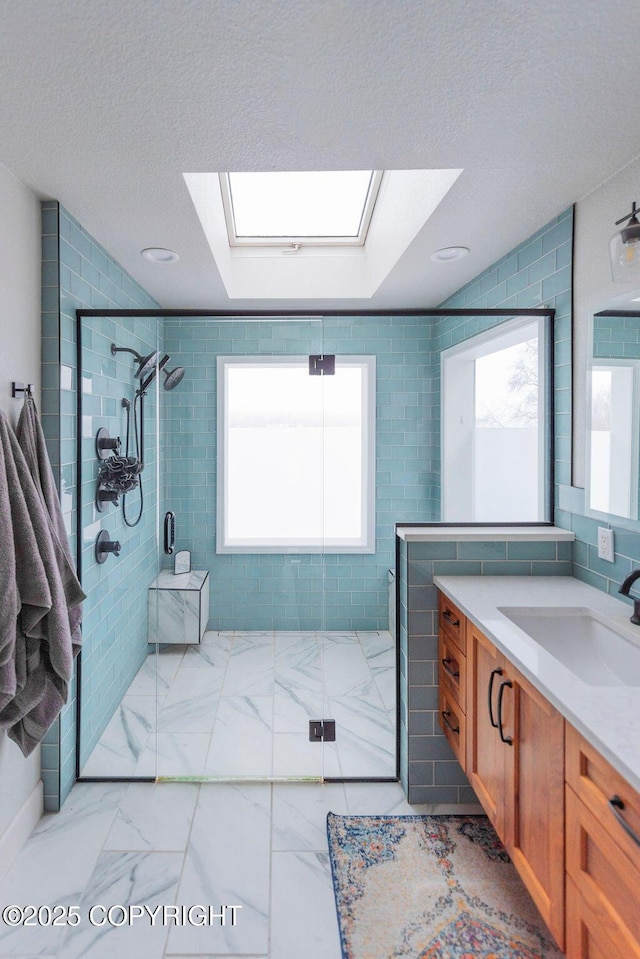 bathroom featuring vanity, a shower with shower door, a textured ceiling, and a skylight