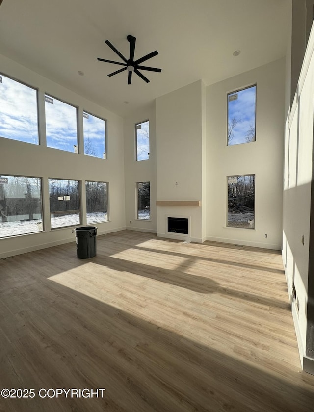 unfurnished living room with light wood finished floors, a fireplace, a high ceiling, and baseboards