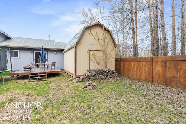 back of property featuring a trampoline, a deck, a storage unit, and a lawn