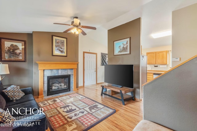 living room with a tiled fireplace, ceiling fan, light hardwood / wood-style flooring, and lofted ceiling