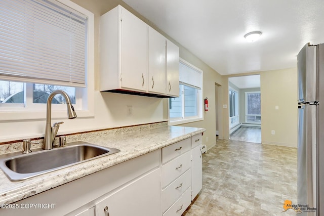 kitchen with white cabinetry, stainless steel refrigerator, and sink