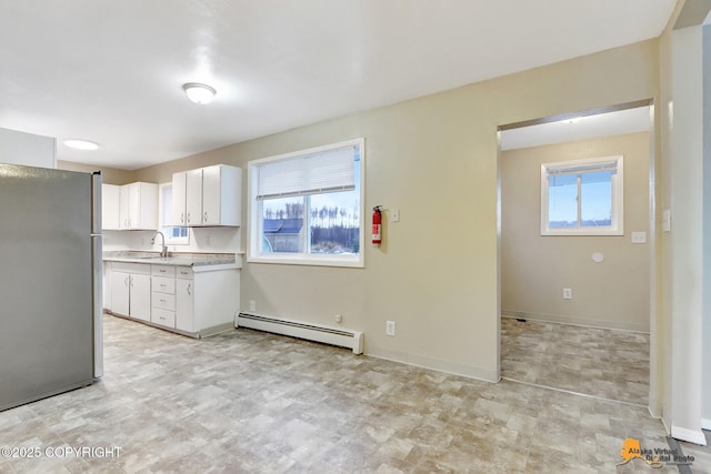 kitchen with sink, stainless steel fridge, baseboard heating, a healthy amount of sunlight, and white cabinetry