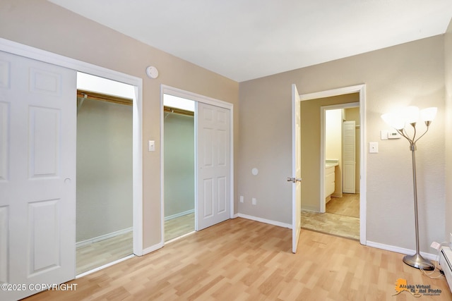 unfurnished bedroom with hardwood / wood-style floors, a baseboard radiator, and multiple closets