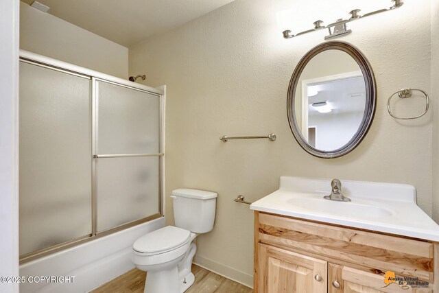 full bathroom featuring shower / bath combination with glass door, hardwood / wood-style floors, vanity, and toilet