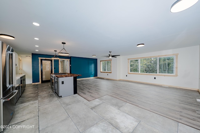 kitchen with pendant lighting, ceiling fan, a kitchen island, butcher block counters, and stainless steel appliances