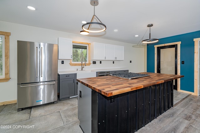 kitchen featuring wooden counters, appliances with stainless steel finishes, white cabinets, and hanging light fixtures