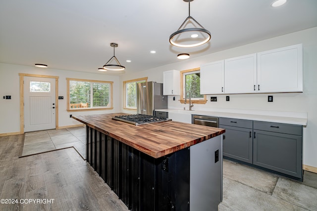 kitchen featuring wood counters, appliances with stainless steel finishes, decorative light fixtures, a kitchen island, and white cabinetry