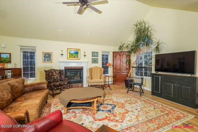 living room with a brick fireplace, light hardwood / wood-style flooring, ceiling fan, and vaulted ceiling