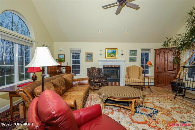 living room featuring a brick fireplace, light wood-type flooring, ceiling fan, and vaulted ceiling