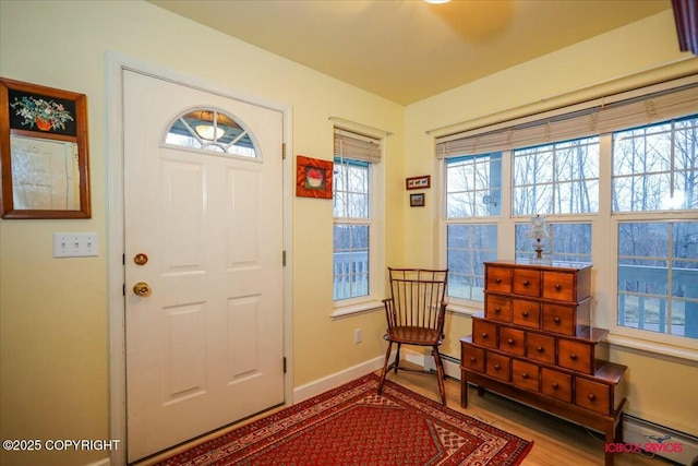 foyer entrance featuring baseboard heating, a healthy amount of sunlight, and light hardwood / wood-style floors