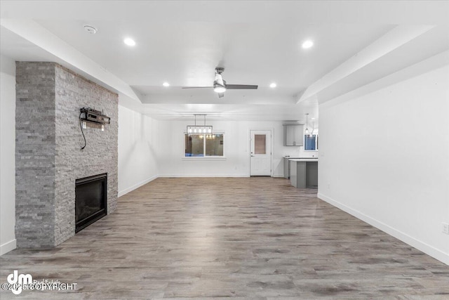 unfurnished living room with ceiling fan, a raised ceiling, wood-type flooring, and a fireplace