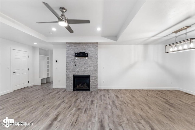 unfurnished living room featuring a fireplace, light wood-type flooring, a raised ceiling, and ceiling fan