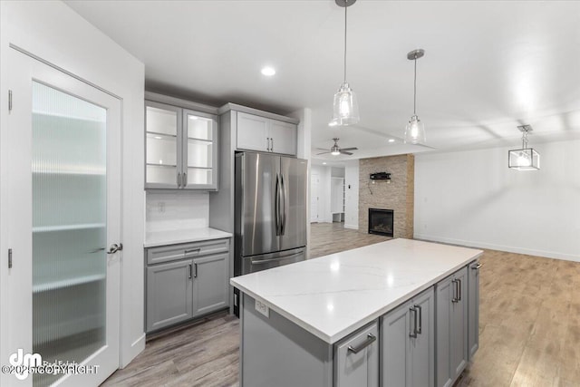 kitchen featuring stainless steel fridge, a stone fireplace, ceiling fan, and pendant lighting