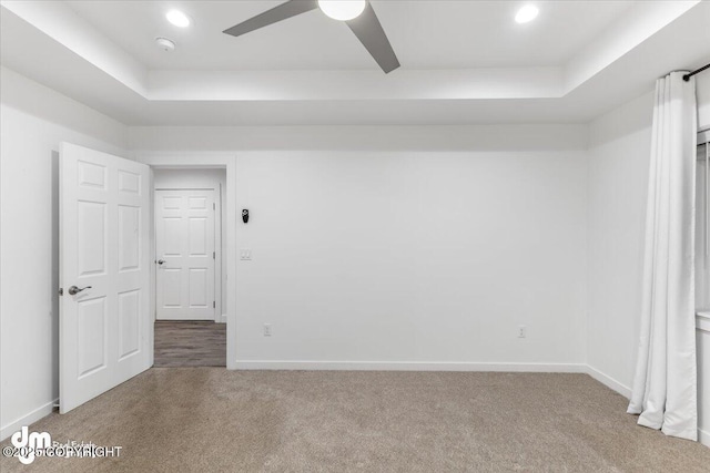 carpeted spare room featuring a raised ceiling and ceiling fan