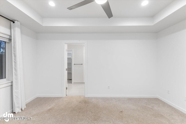 empty room featuring light carpet, a raised ceiling, and ceiling fan