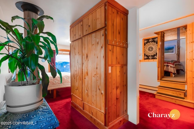 hallway with dark colored carpet, wood walls, and a baseboard radiator