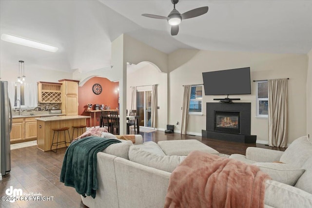 living room featuring lofted ceiling, a tile fireplace, sink, ceiling fan, and dark hardwood / wood-style flooring