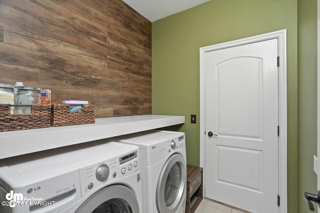 clothes washing area featuring washer and dryer, light tile patterned floors, and wooden walls